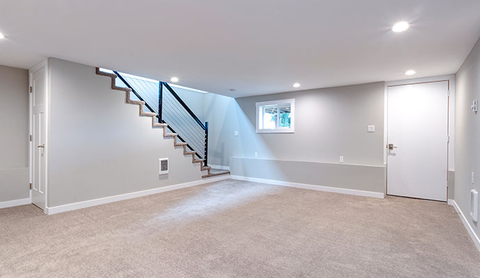 A clean, well-lit finished basement with grey walls and new carpeting